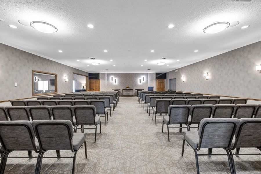 Empty conference room with rows of gray chairs facing a front stage and ceiling lights