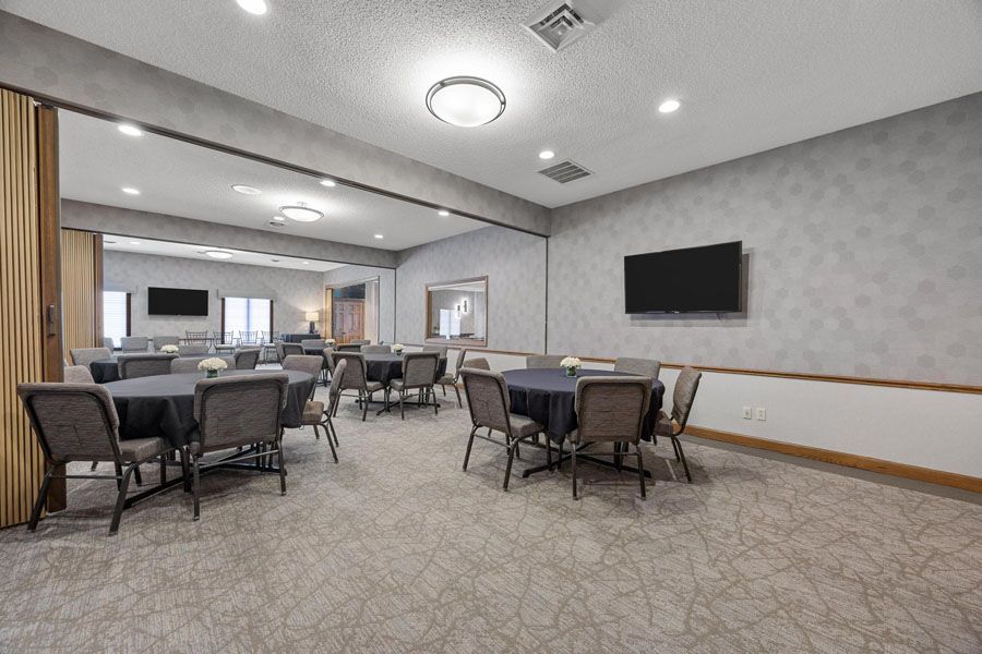 Empty conference room with tables and chairs, wall-mounted TV, and carpeted floor