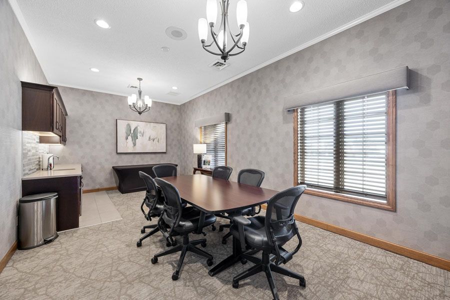 Conference room with dark wood table, black chairs, chandelier lights, and window blinds.