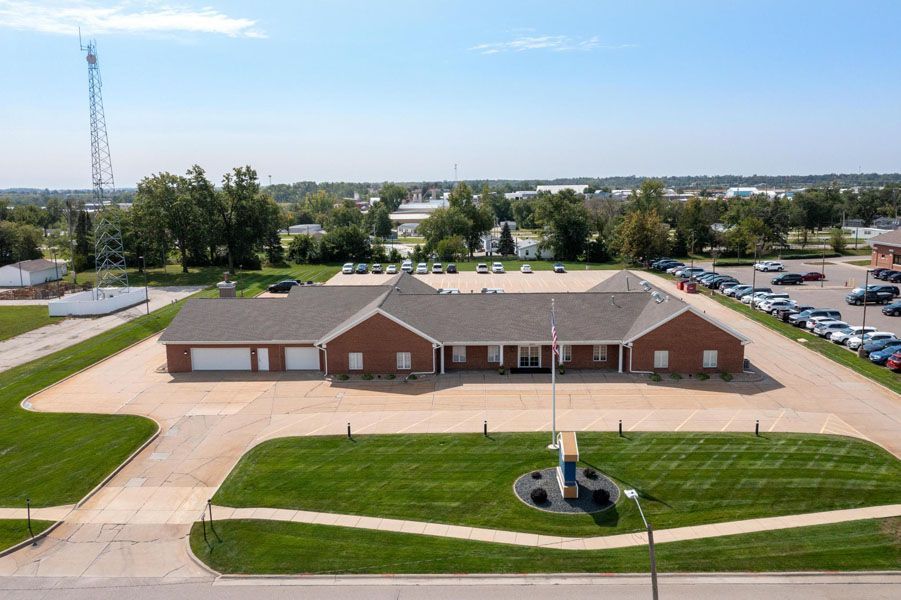 Aerial view of a brick community building with a large parking lot and landscaped grounds under a clear sky