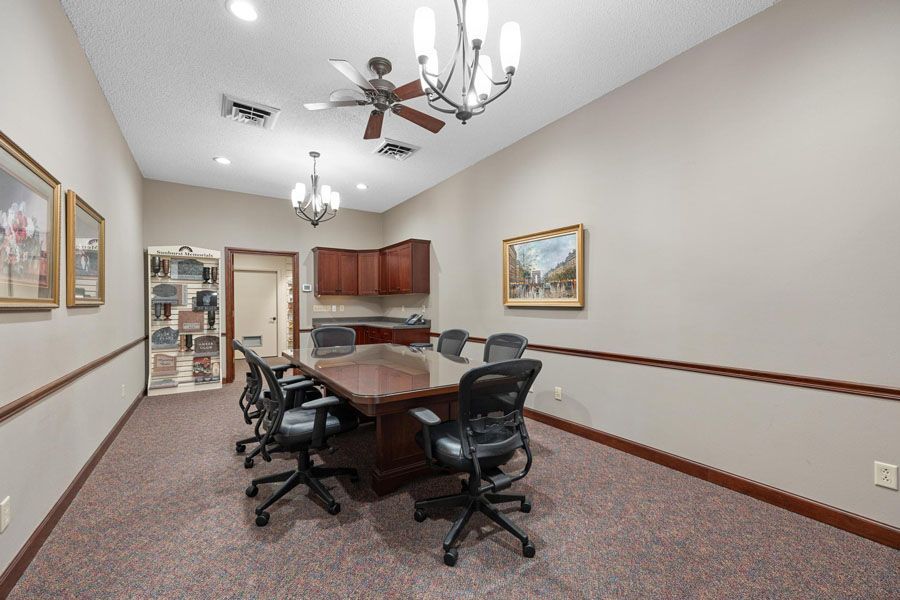 Conference room with oval table, rolling chairs, wall art, and ceiling fan under recessed lighting.