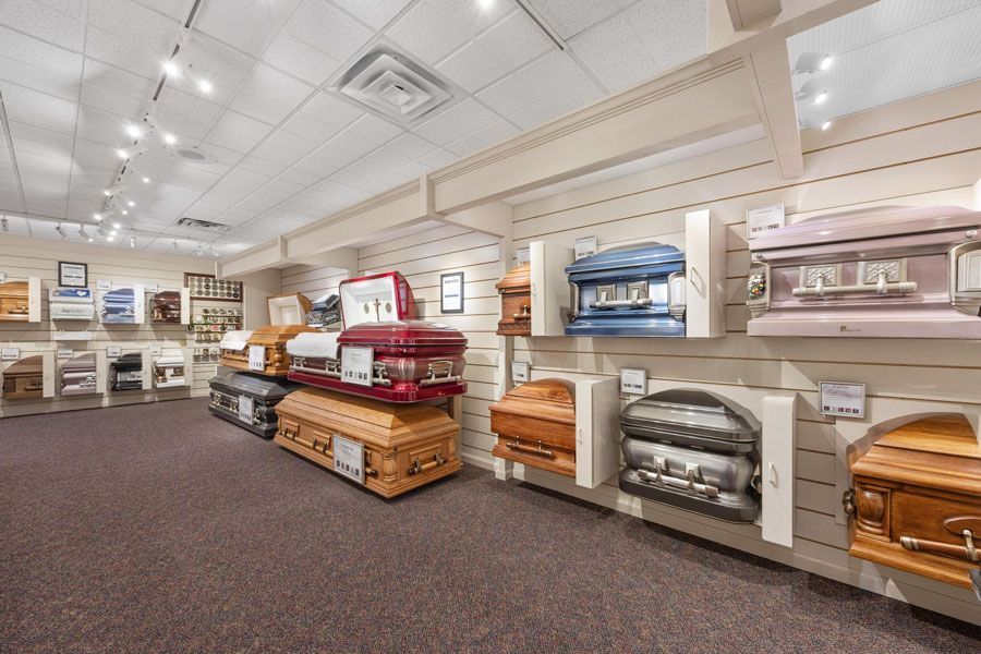 Display room with rows of decorative caskets on shelves and tables under bright ceiling lights