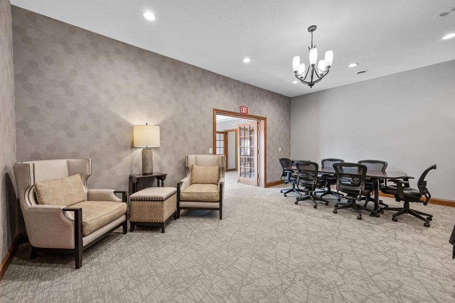 Bright lounge with beige chairs, floor lamp, carpet, chandelier, and a row of black exercise machines.