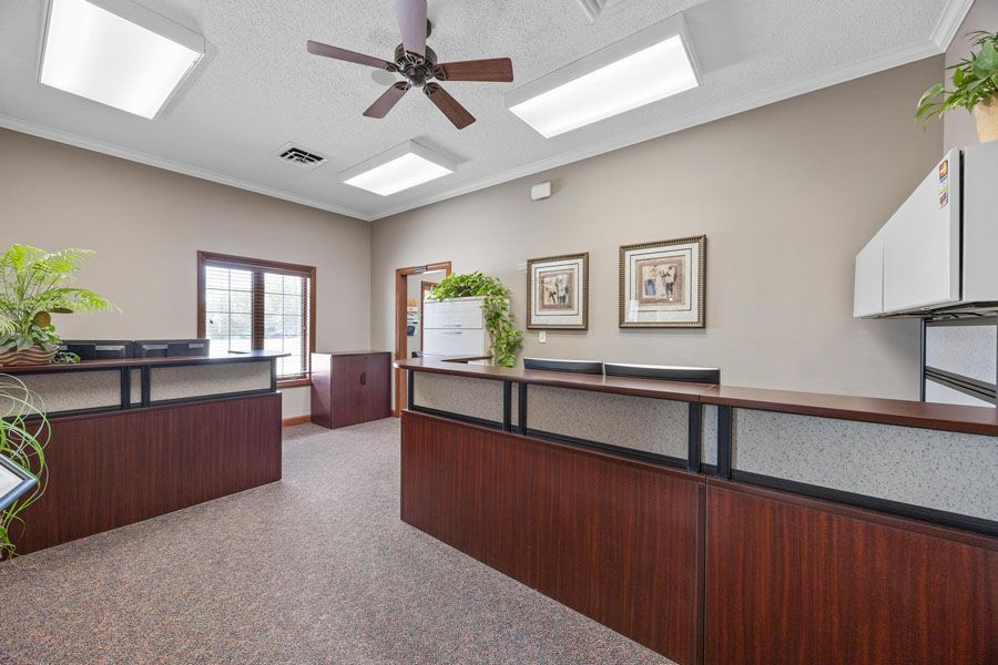 Empty office reception area with wood counters, carpet, ceiling fan, and framed wall art