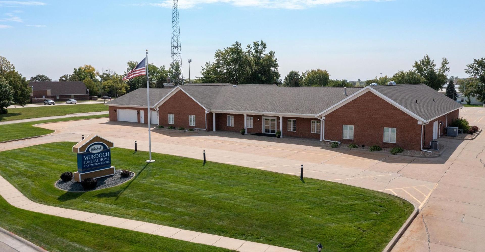 A brick office building with a sign, surrounded by a parking lot and green lawn on a sunny day