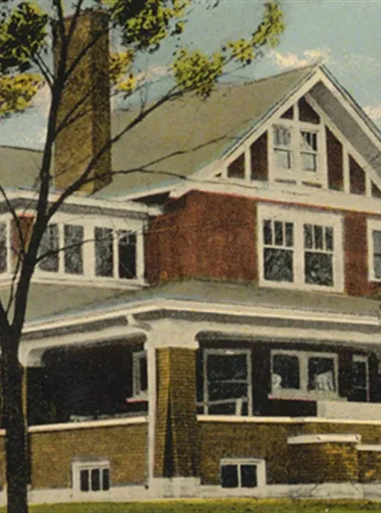 Large Craftsman-style house with a front porch, white trim, and a steep gabled roof under trees
