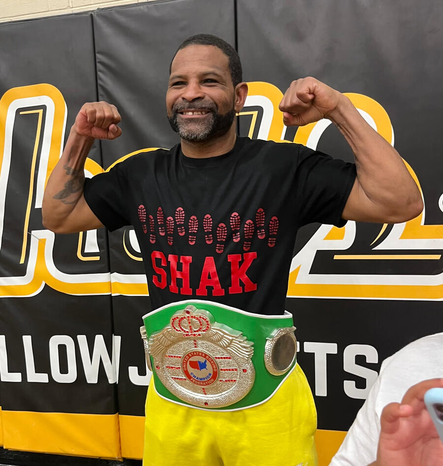 Man flexing arms, wearing a championship belt and