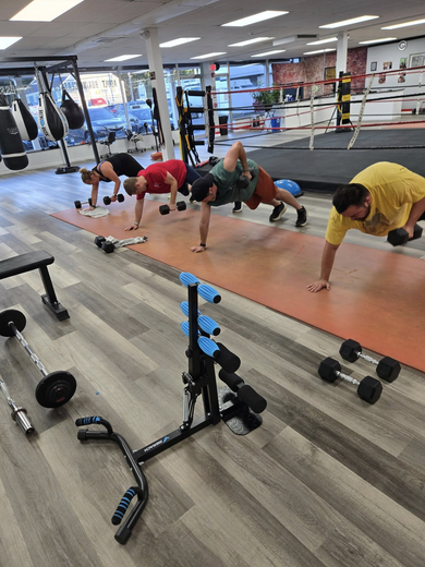 People exercising with dumbbells in a gym. They are doing push-ups.