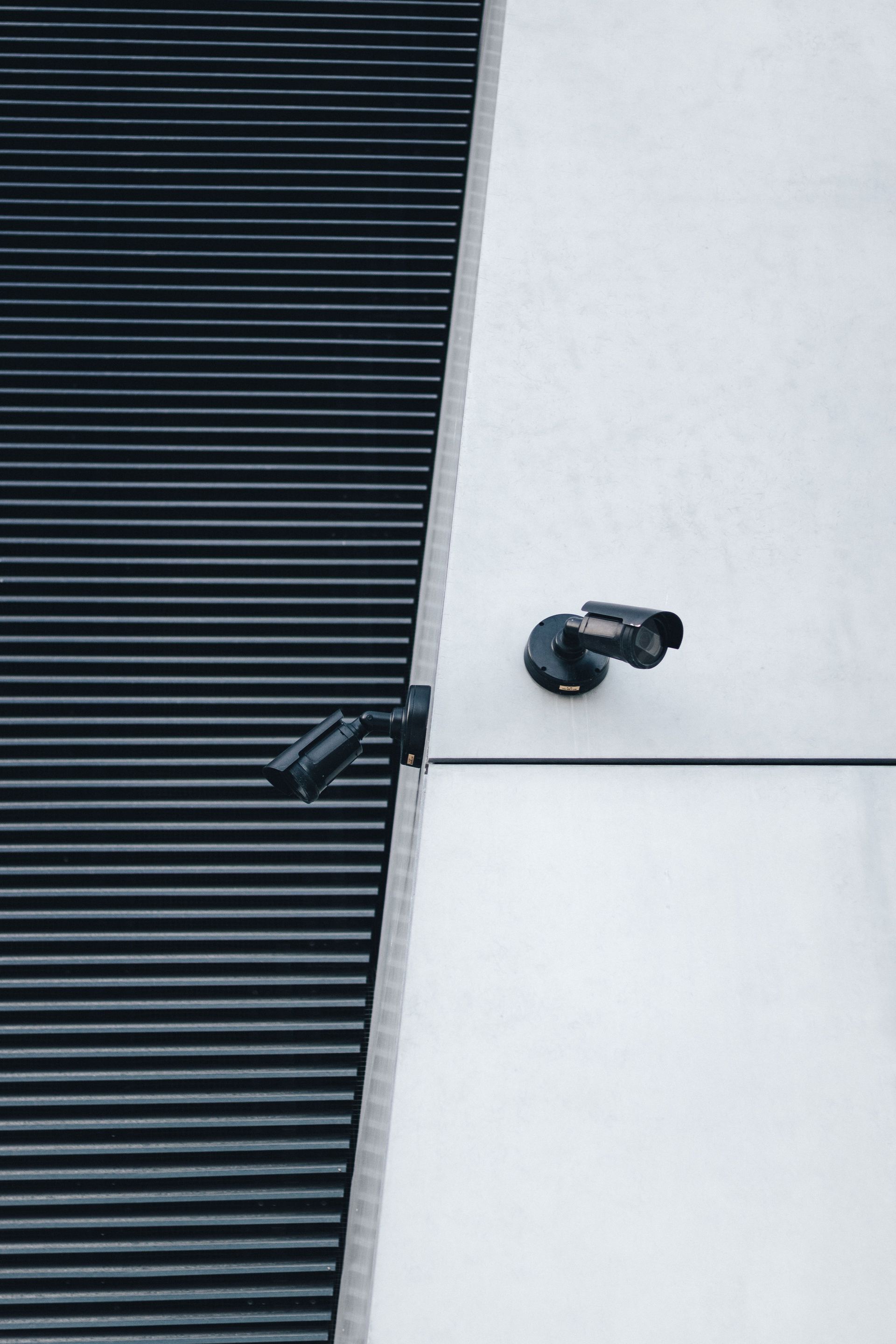 Cámara de seguridad negra montada en una pared blanca junto a un panel oscuro con celosías.