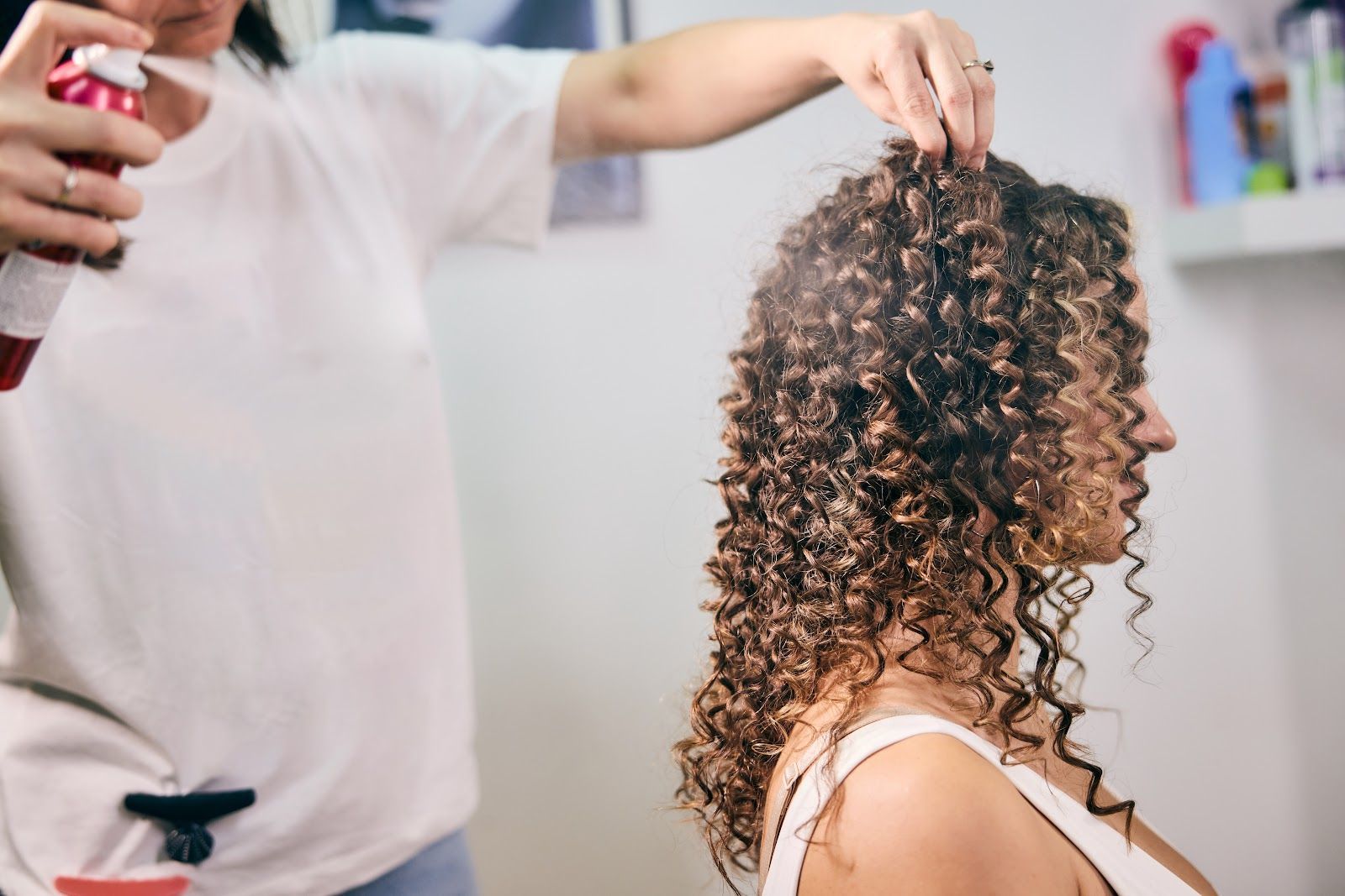 Stylist spraying product on a seated client’s curly hair in a salon