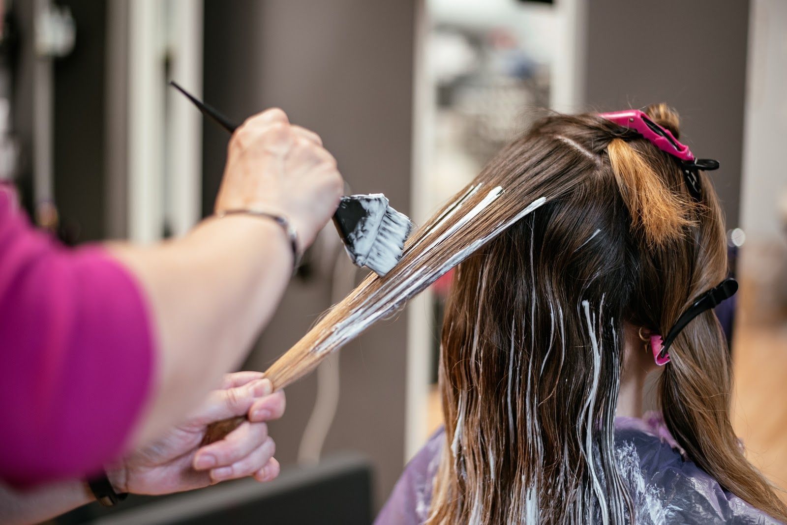 Hair stylist applying blonde highlights to long brown hair in a salon