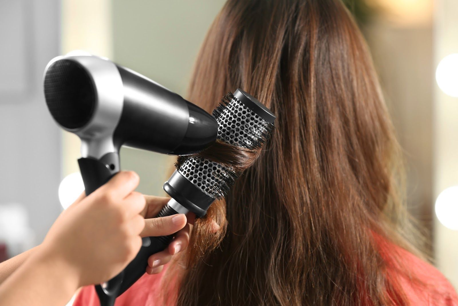 Blow-drying long brown hair with a round brush in a salon setting