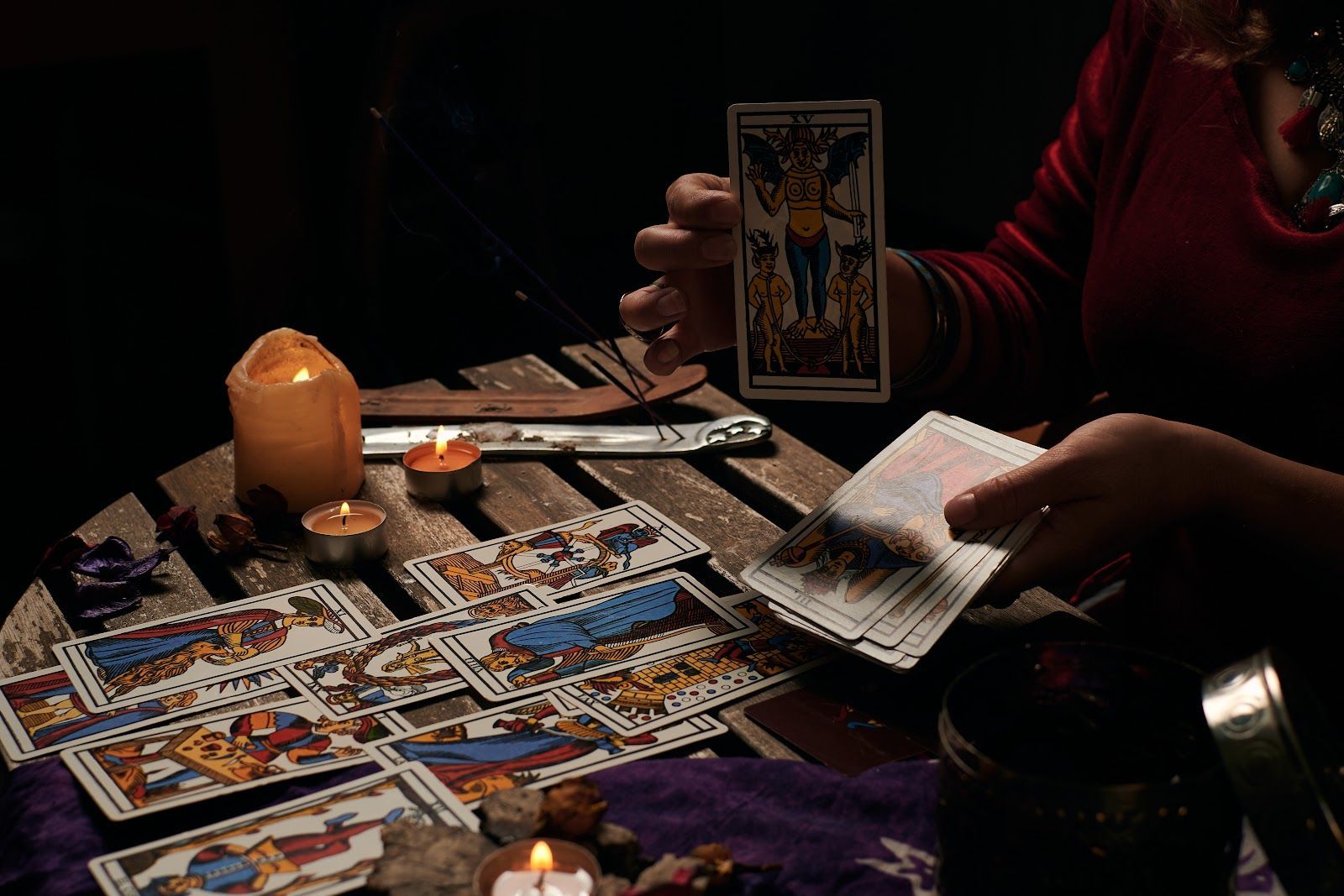 Tarot cards spread on a candlelit table as a person flips through a card deck.