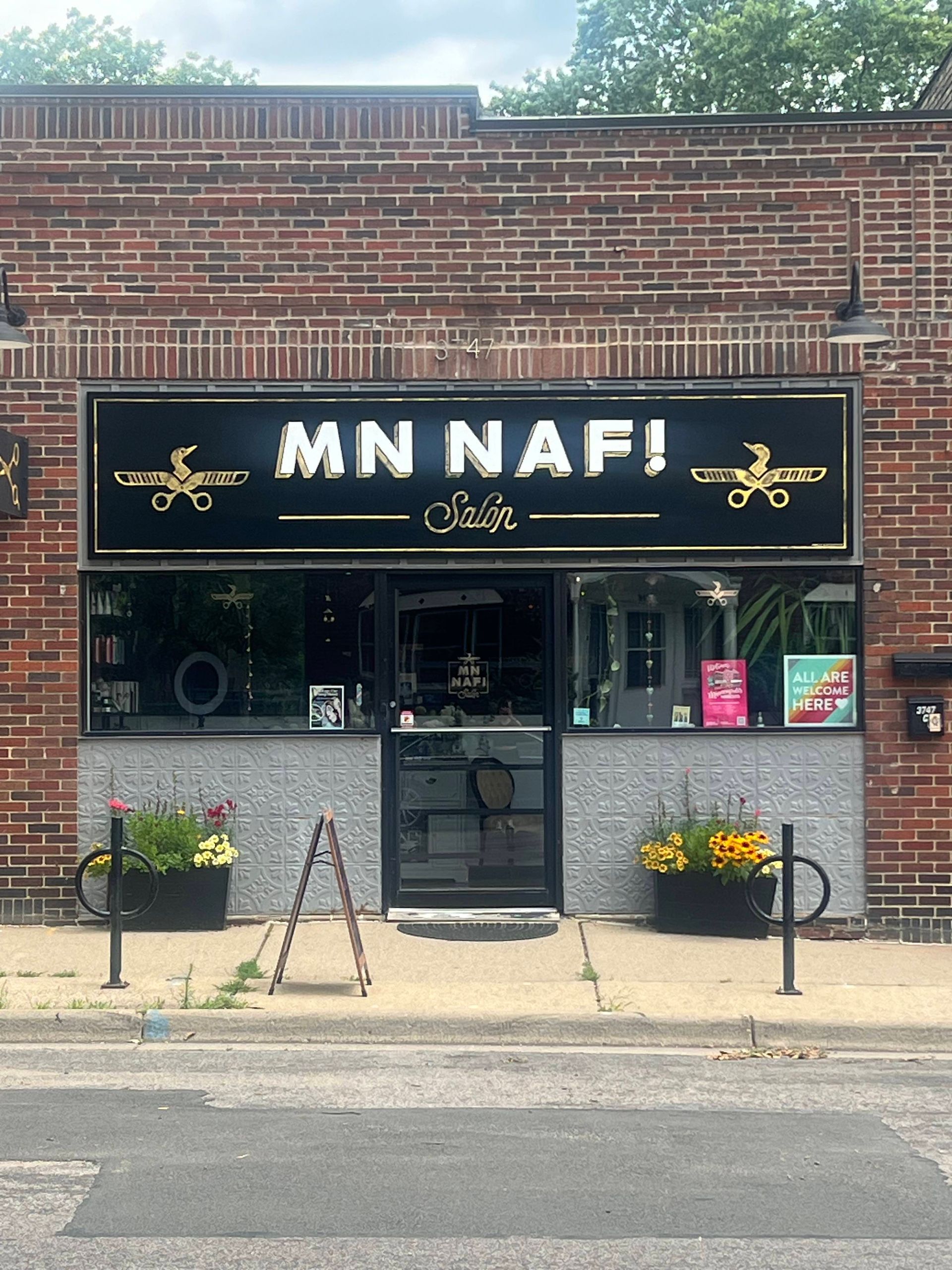 MN NAF! salon storefront with brick facade, black sign, glass door, and flower boxes.