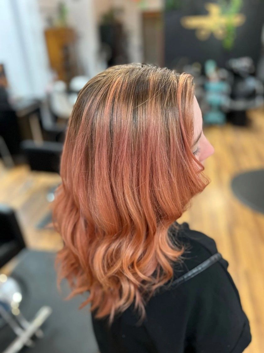 Woman with peach-colored hair in a salon, wavy with darker roots, side profile.