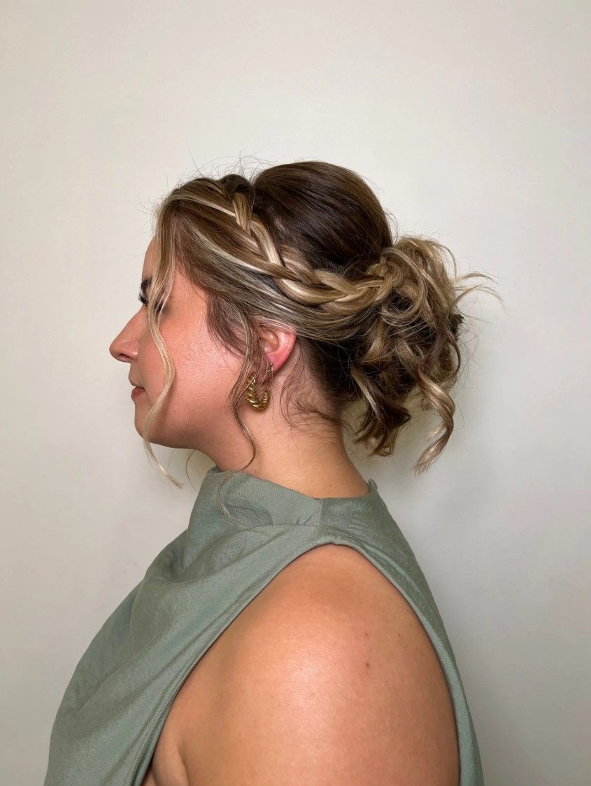 Woman with wavy hair in a braided updo, wearing a green top, side profile.