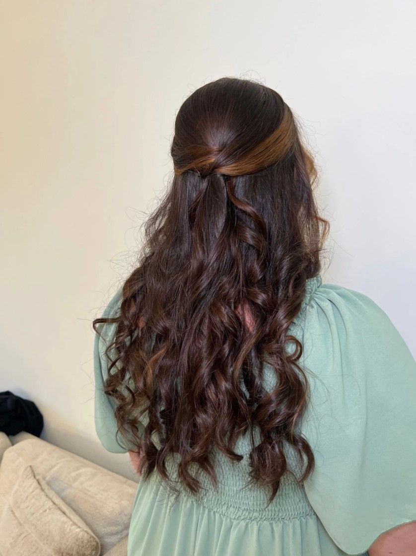 Woman with long, wavy brown hair in a half-up twist hairstyle, wearing a sage green dress.