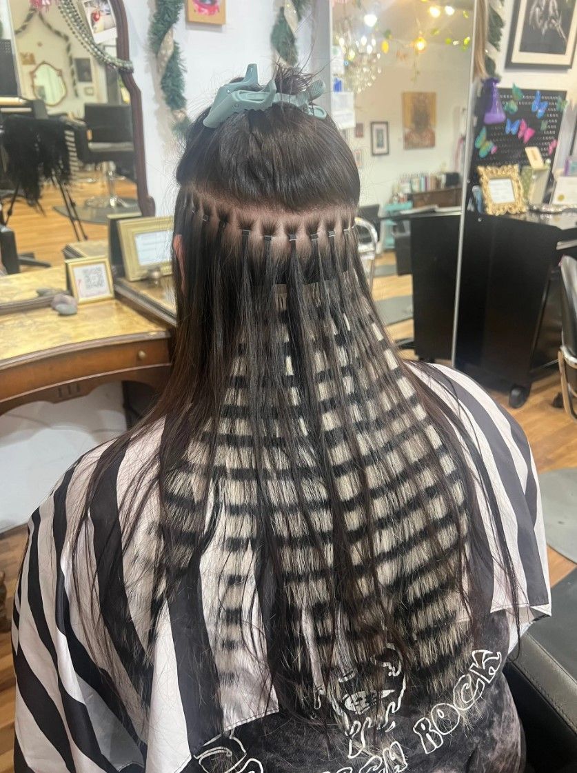 Person with hair extensions in a salon chair; hair is sectioned in a grid pattern.
