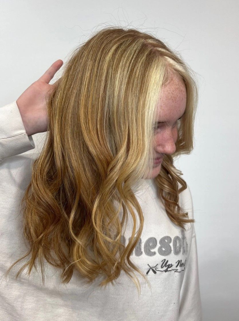 Person with wavy blonde and light brown hair, touching their hair against a white background.