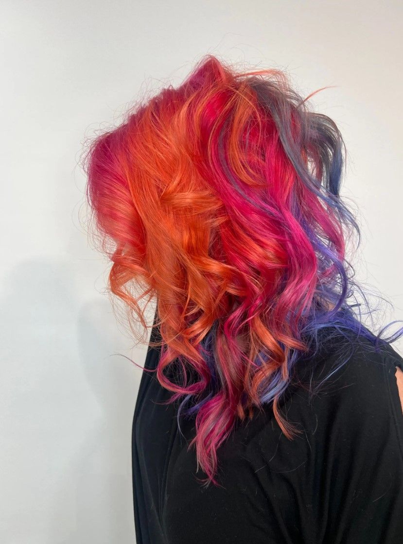 Woman with vibrant, multicolored wavy hair; shades of orange, red, pink, and purple.