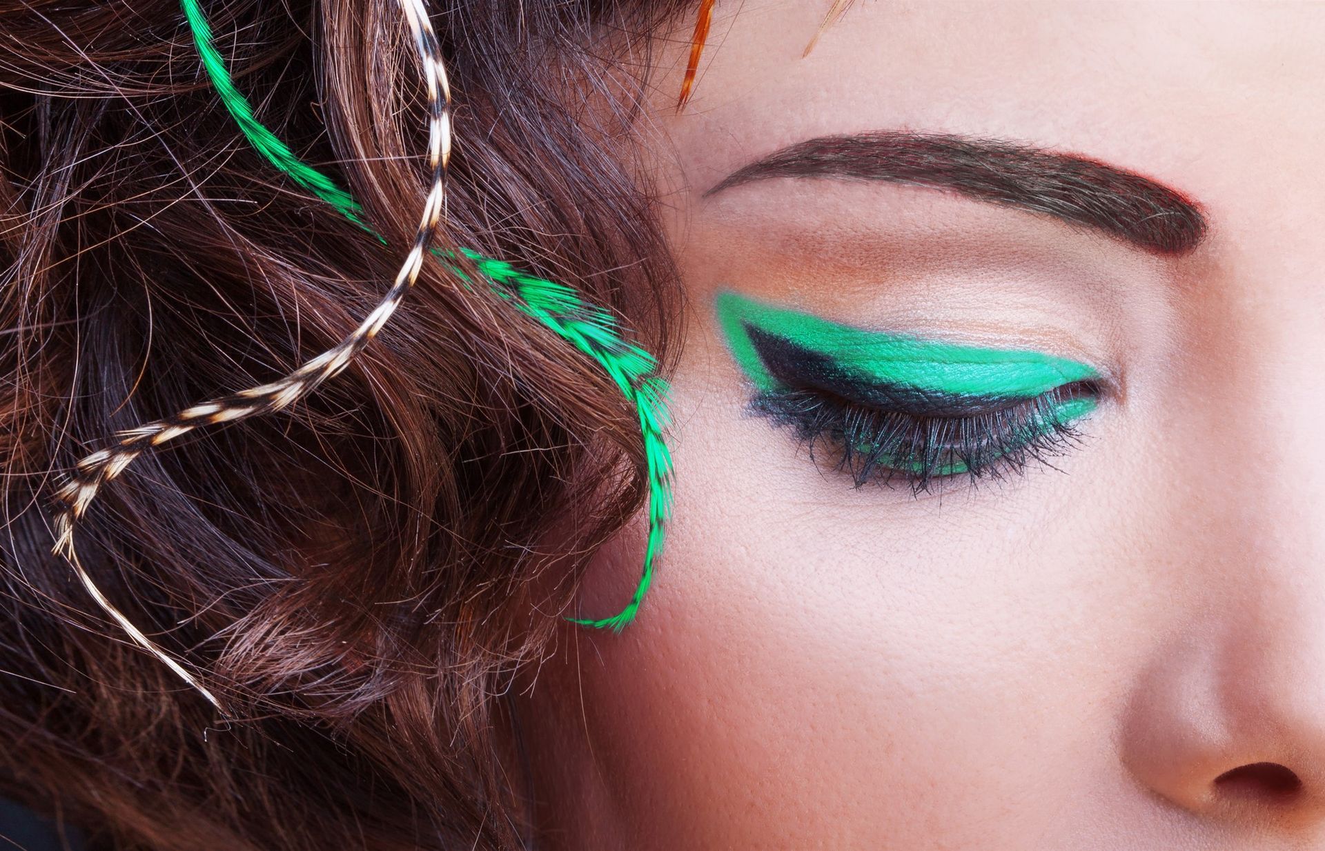 Close-up of eye with dramatic turquoise eyeliner and matching hair accents.