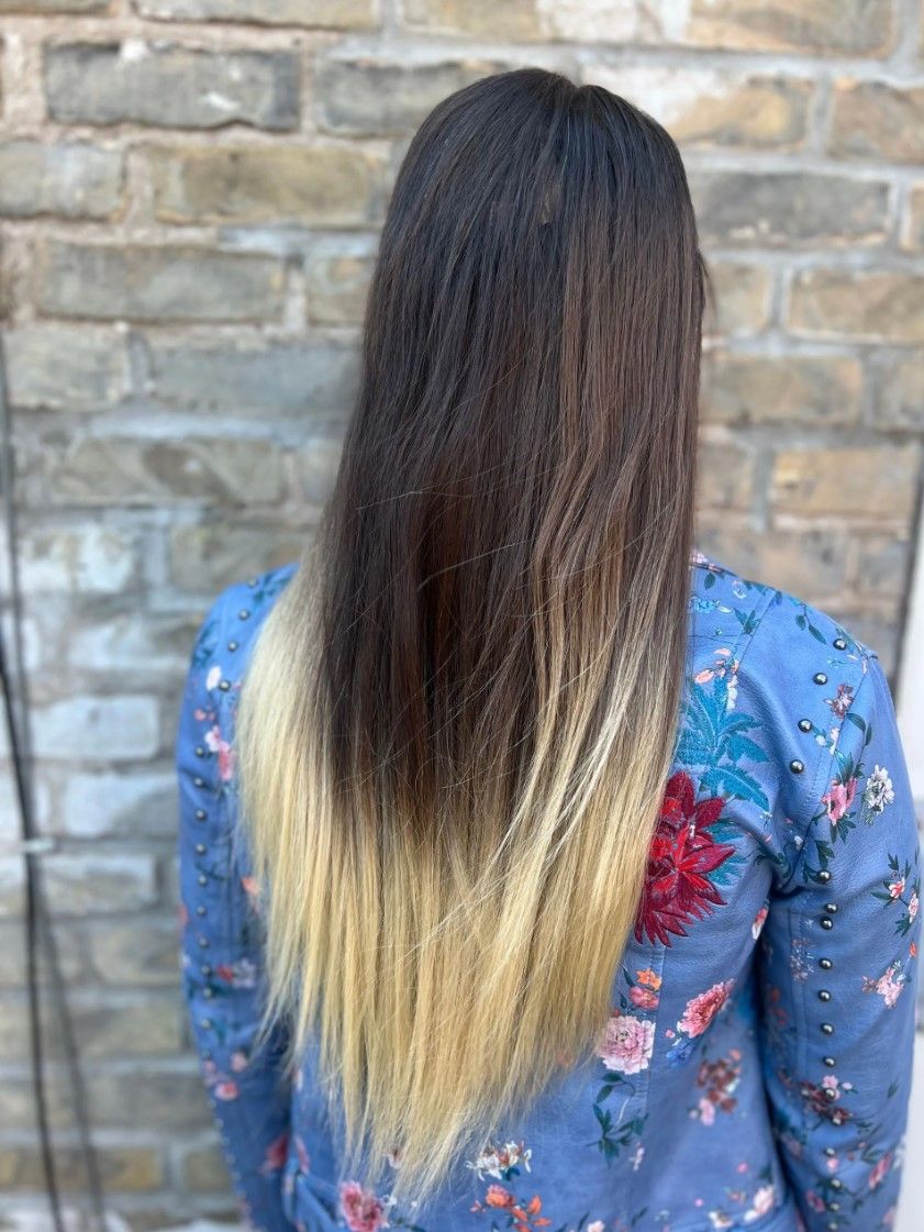Woman with dark hair fading to blonde, standing against a brick wall, wearing a blue floral shirt.