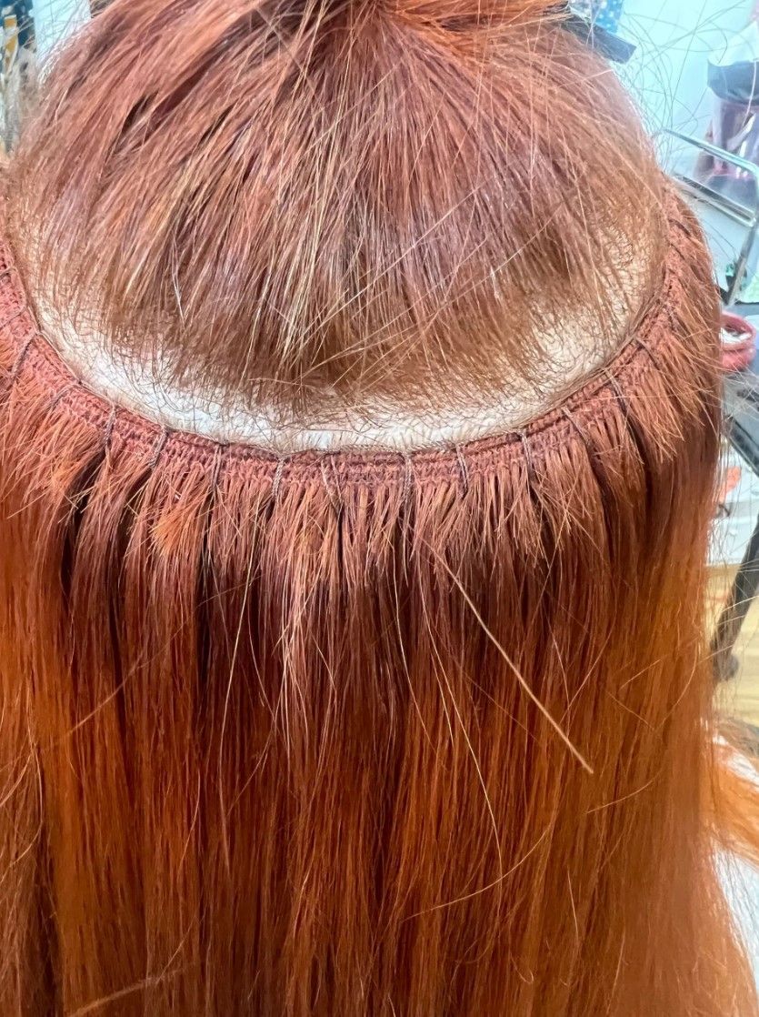 Close-up of red hair with weft extensions sewn in along the head.