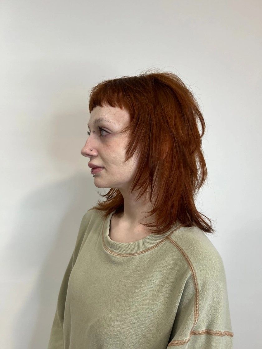 Person with red, layered hair, bangs, and light green sweater.