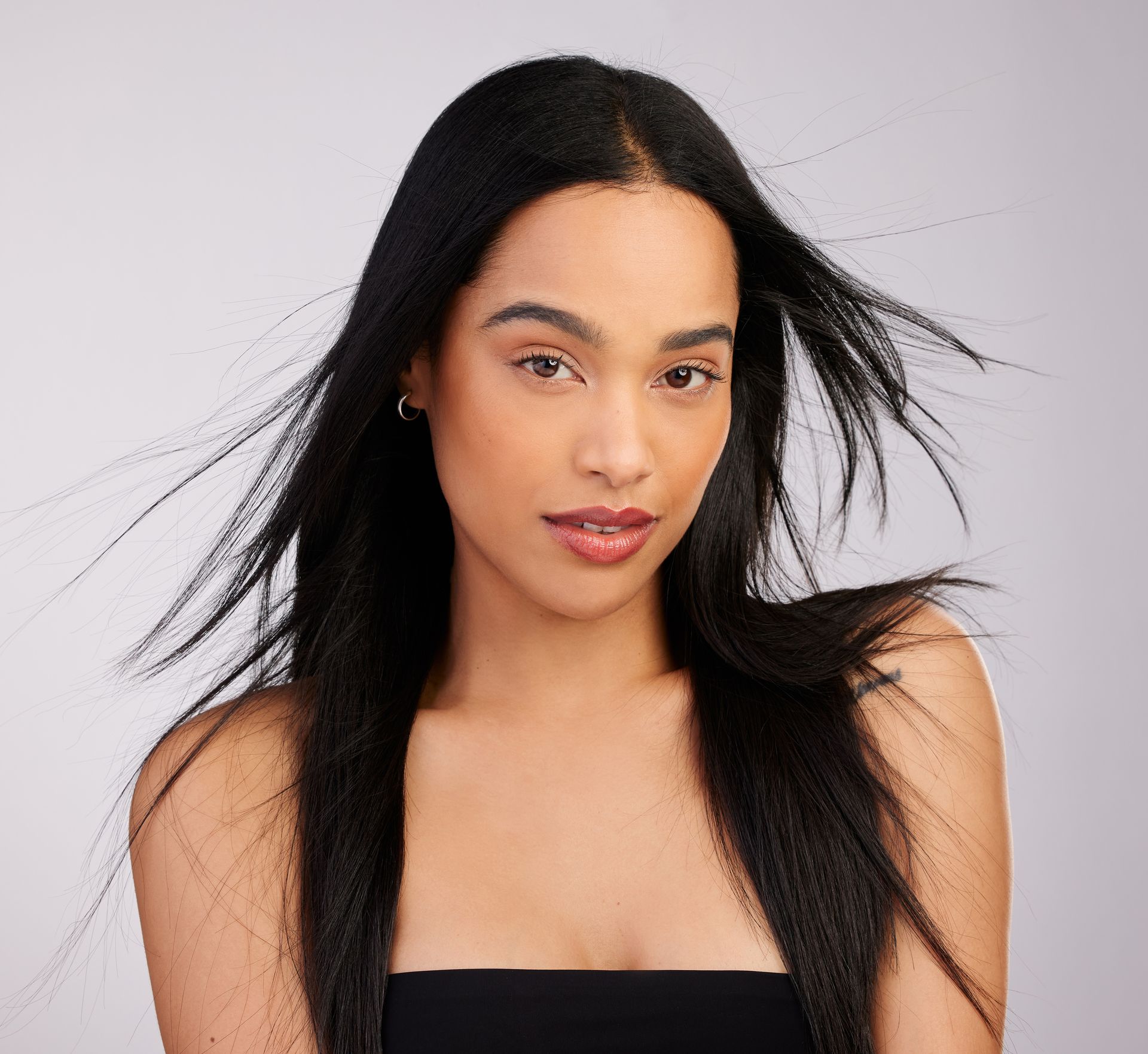 Woman with dark, straight hair, looking at the camera, wearing a black top against a light gray background.