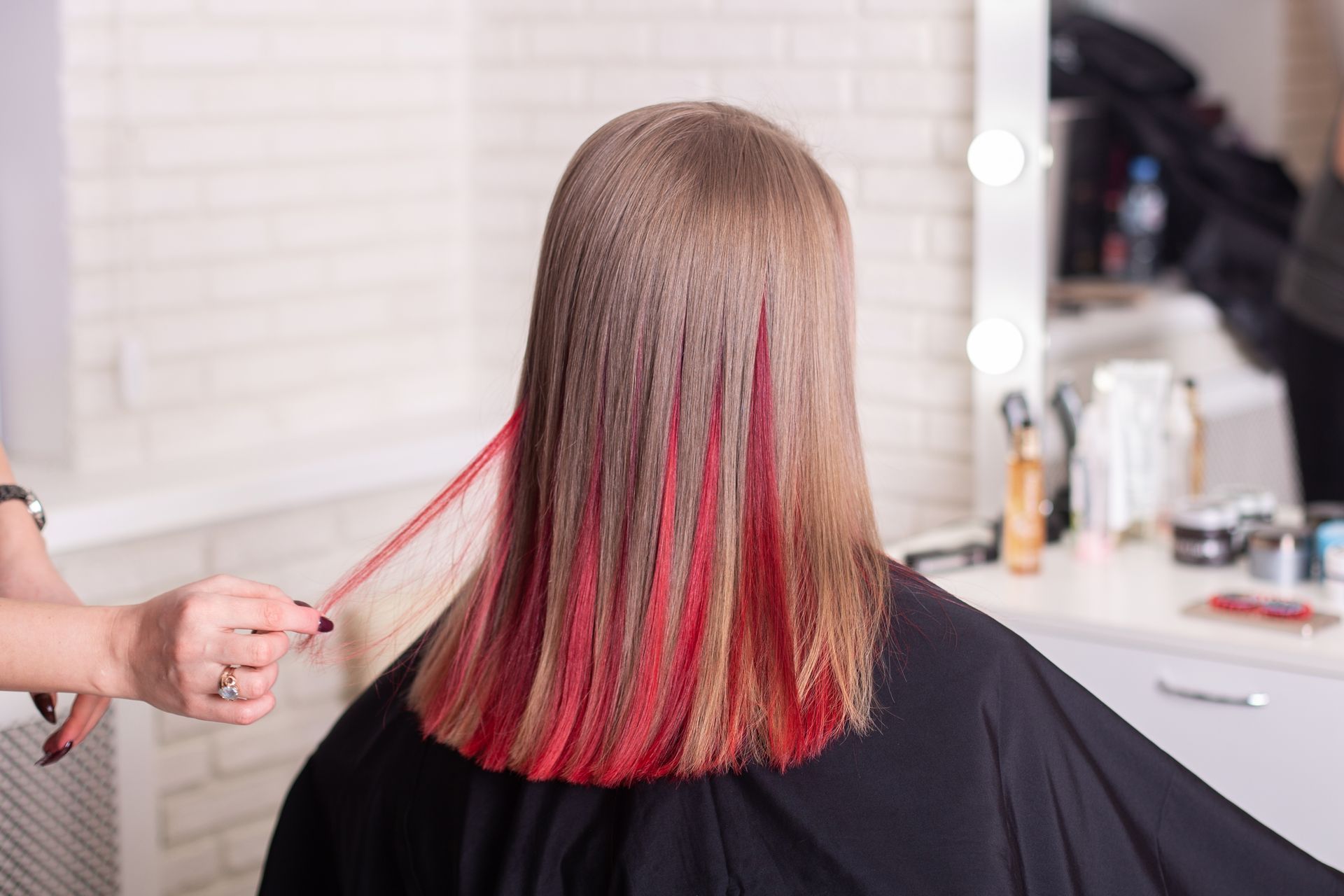 Hairdresser styling long, straight, brown hair with red highlights in a salon.
