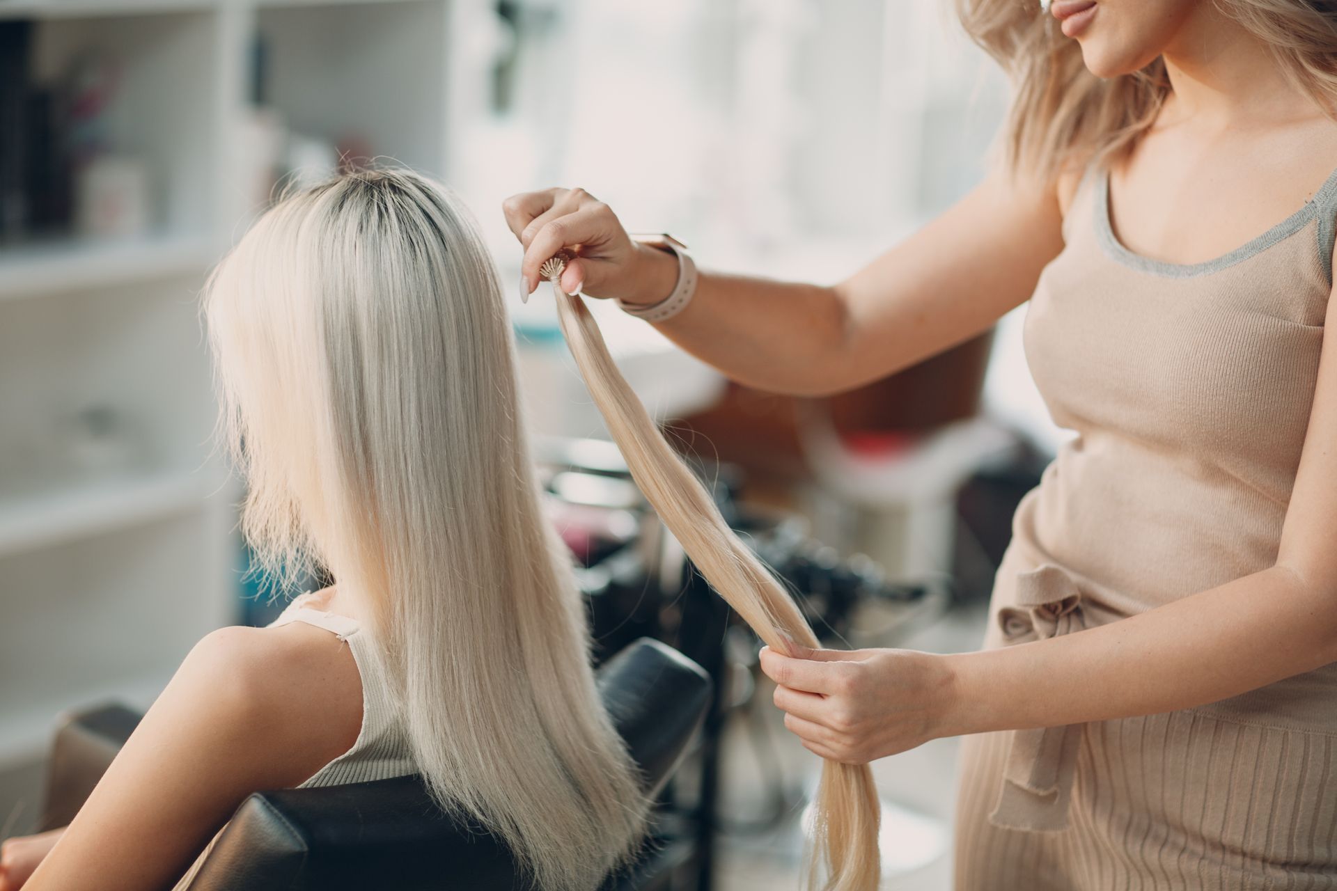 Blonde hair stylist applying hair extensions to a client in a salon.