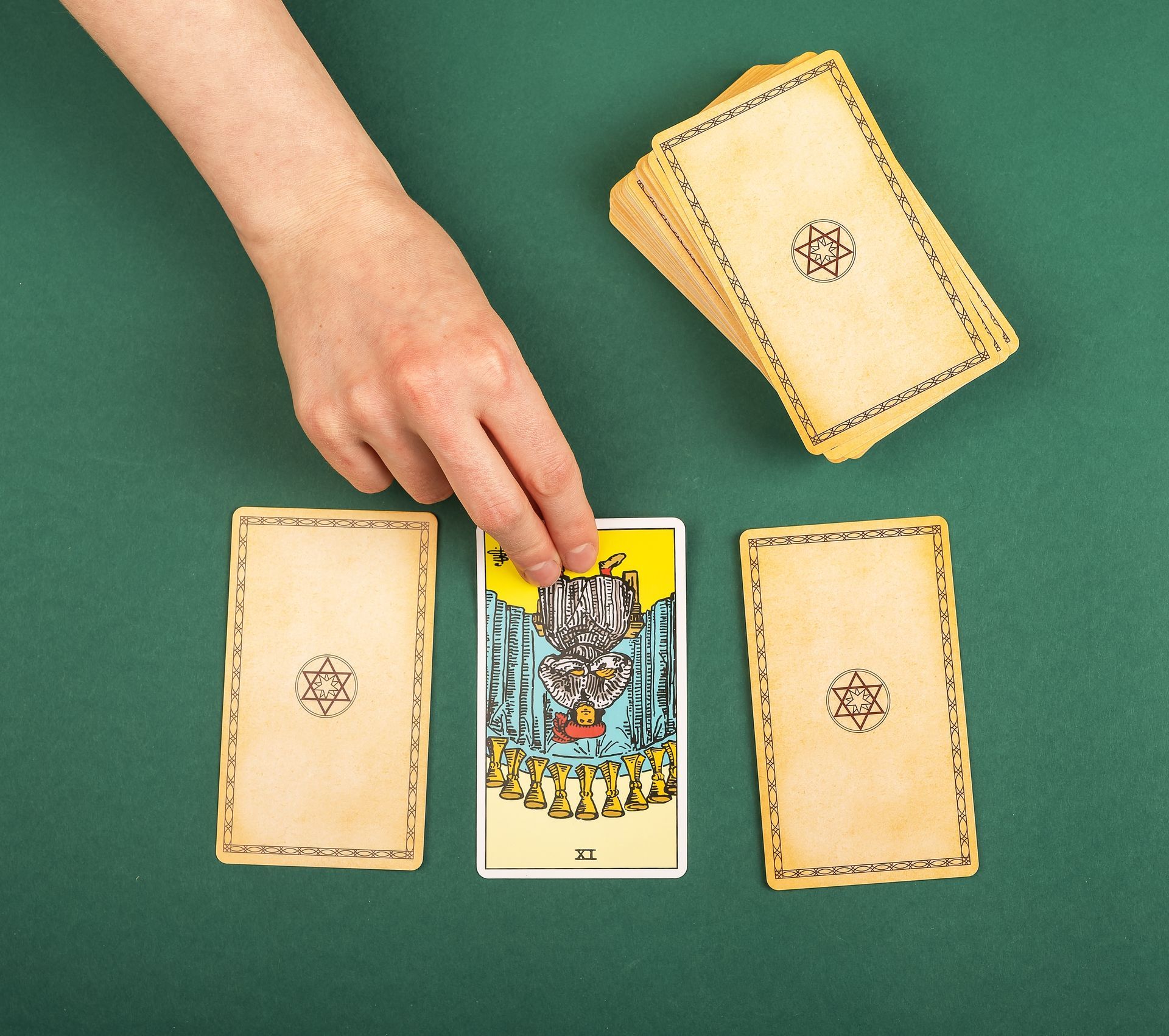 Hand choosing tarot card with two other cards on green surface, deck in the background.