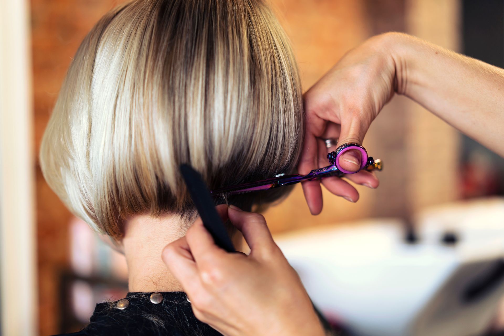 Hairdresser cutting blonde bob hairstyle with scissors.