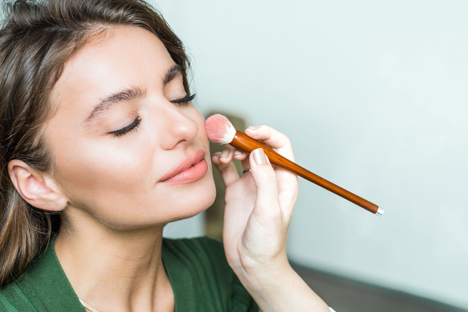 Woman applying makeup with a brush to her cheek, indoors.