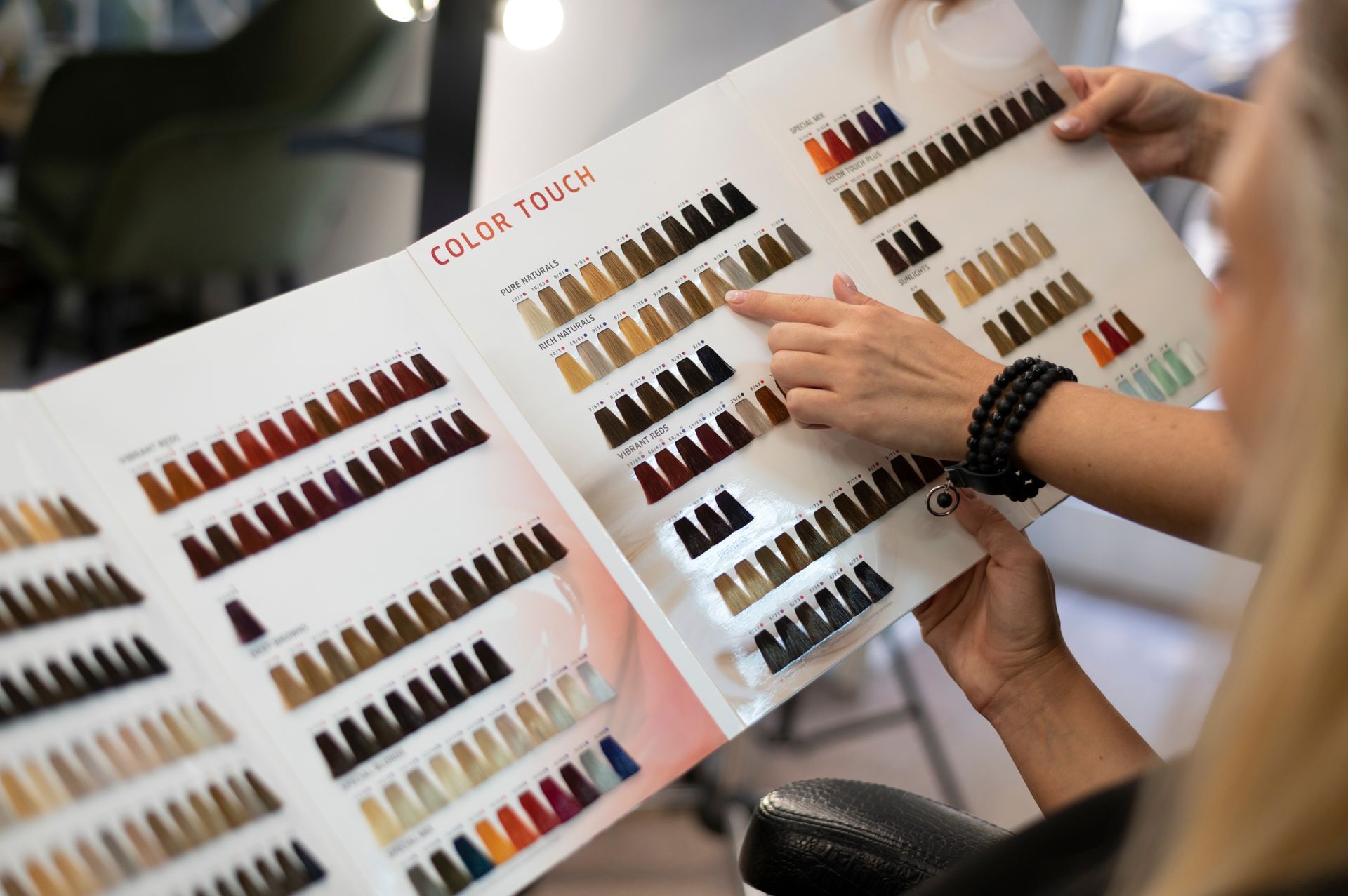 Hands pointing at a hair color chart with various color swatches in a salon setting.