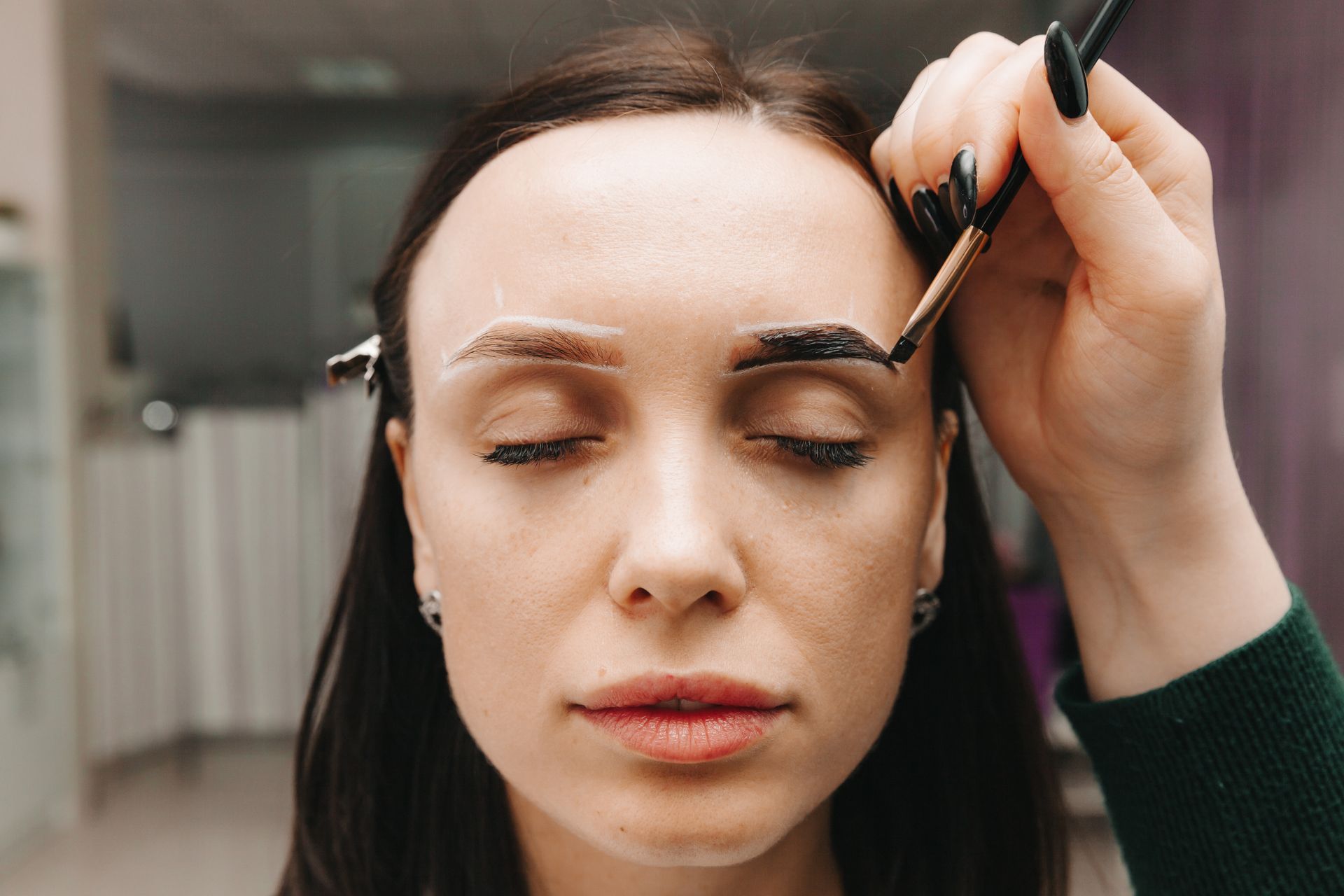 Person receiving eyebrow tinting treatment with a brush in a beauty salon.