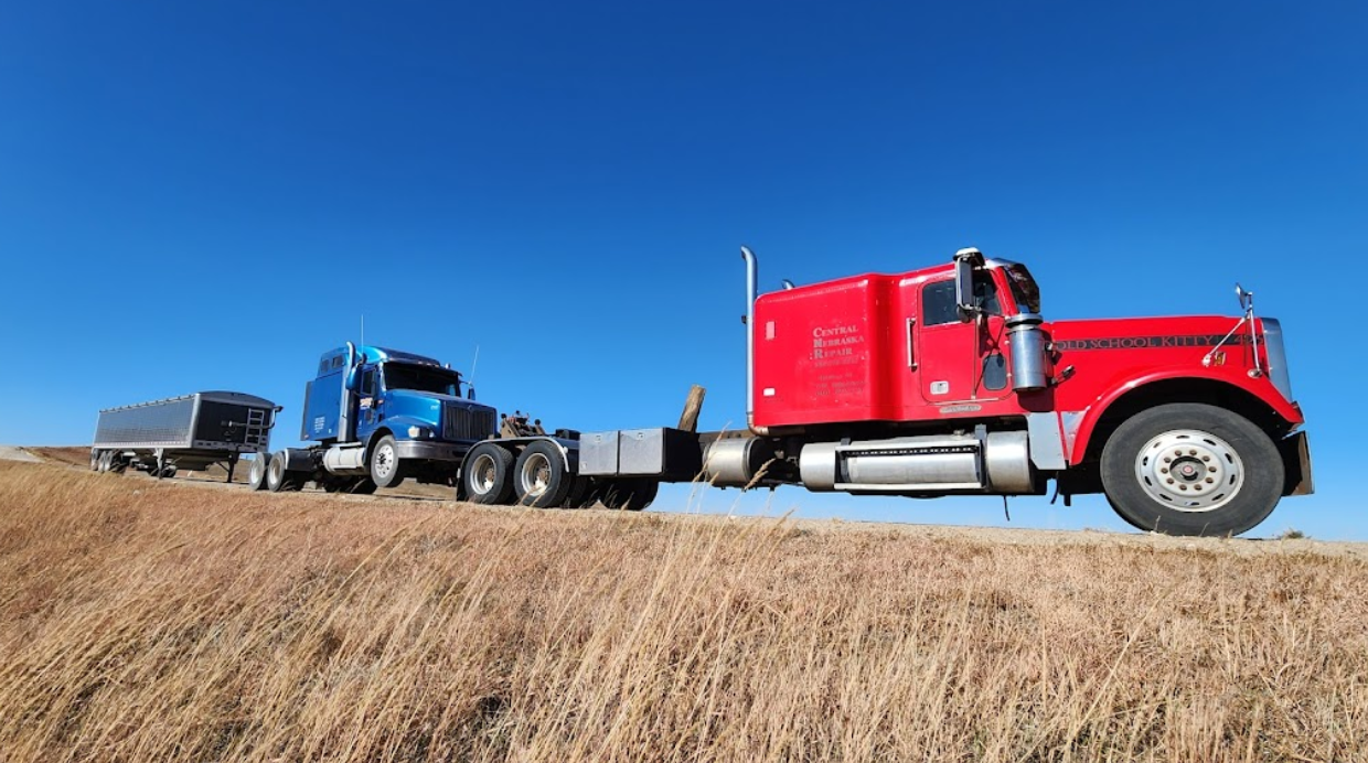 Two semi trucks are driving down a dirt road.
