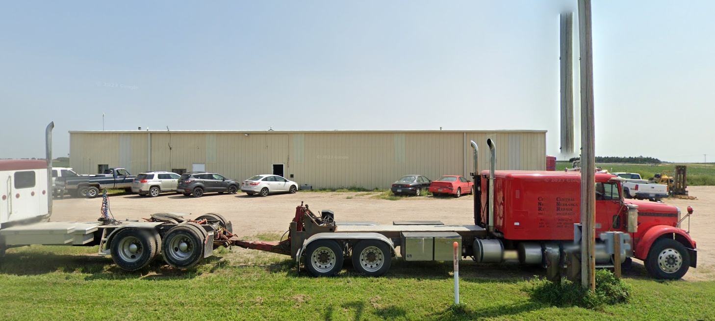 A red semi truck is parked in a grassy field in front of a building.