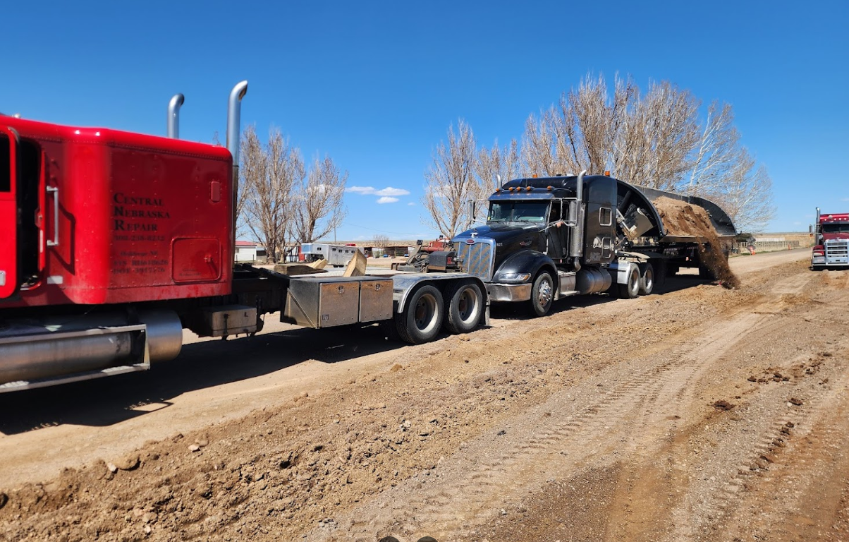 A row of semi trucks are parked on a dirt road.