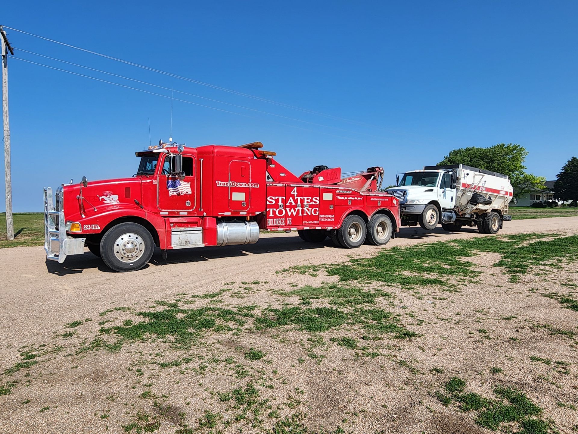 A red States Towing truck towing a white work truck on a gravel lot under a clear blue sky.
