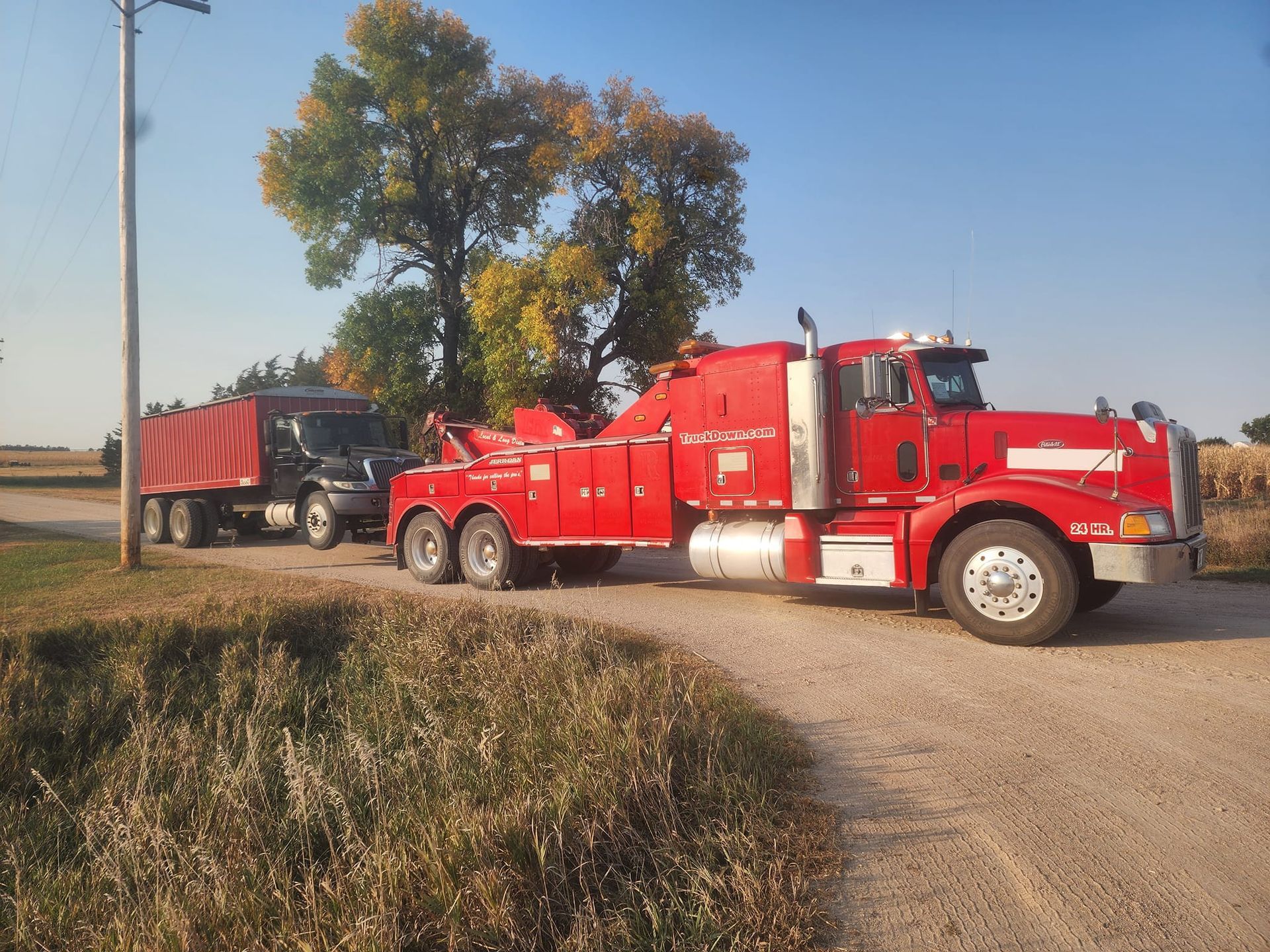 A red tow truck is parked next to a dump truck