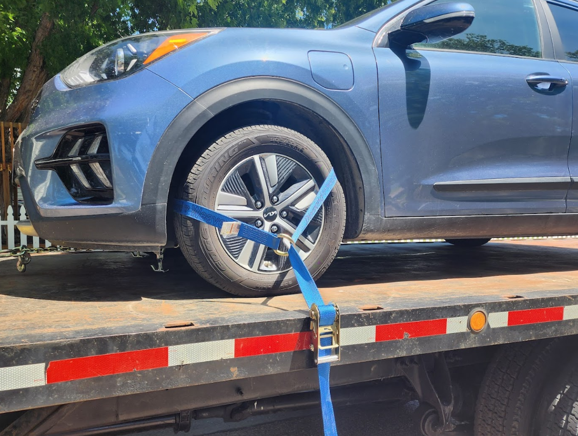 A blue car is sitting on top of a flatbed tow truck.