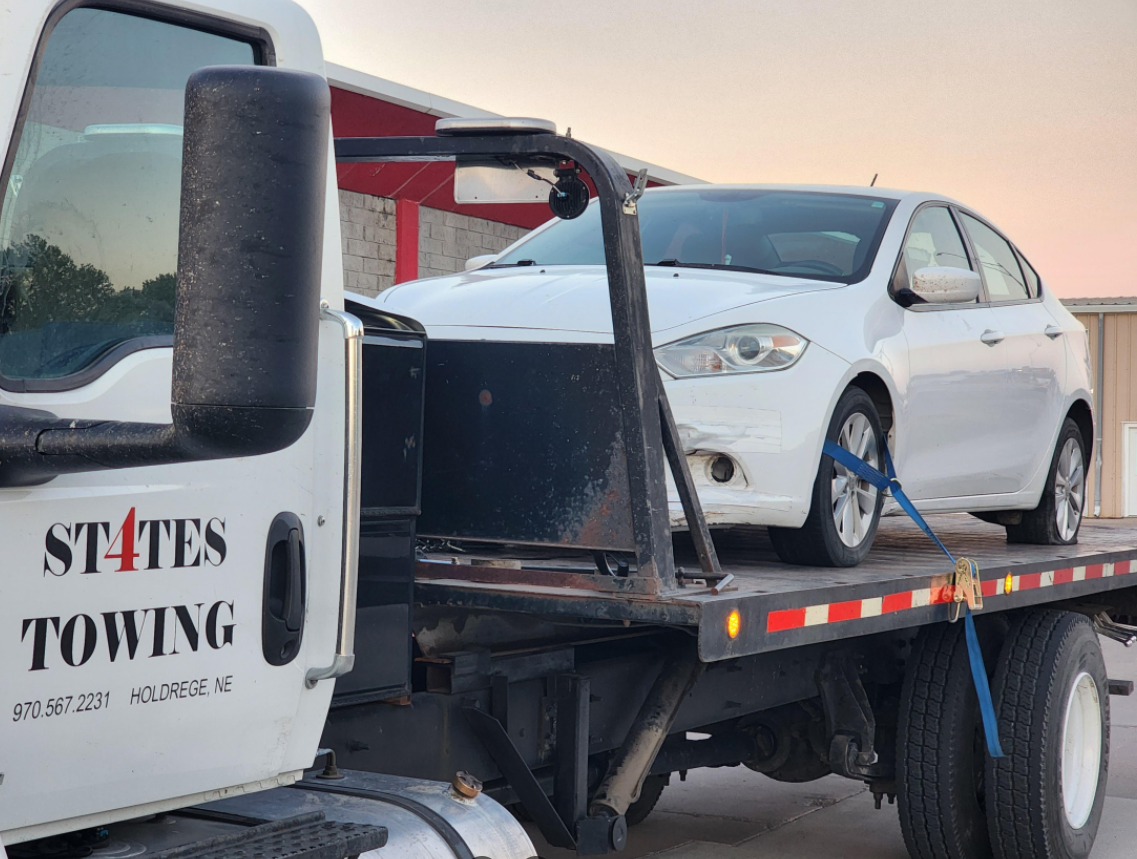 A white car is being towed by a states towing truck.