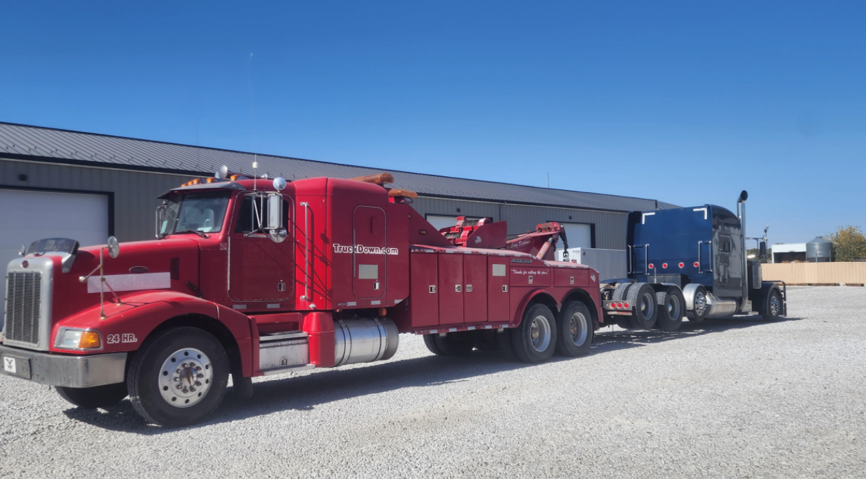A red tow truck is parked next to a blue semi truck.