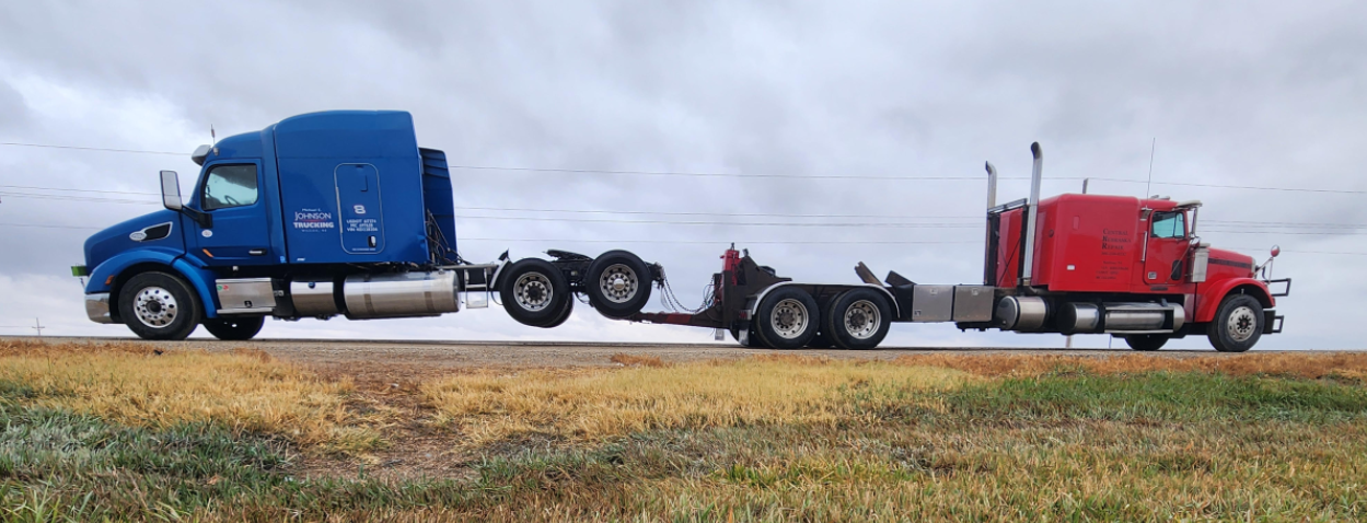 Two semi trucks are driving down a road in a field.