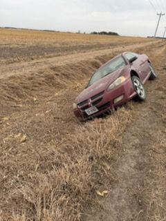 Maroon sedan overturned in a dry roadside ditch beside a rural field.
