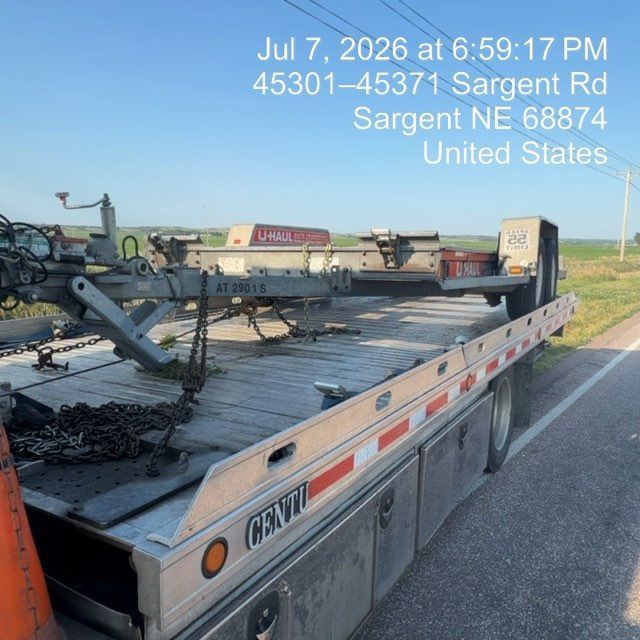 Flatbed trailer hauling farm equipment on a roadside in Sargent, Nebraska, with date and location text overlay.