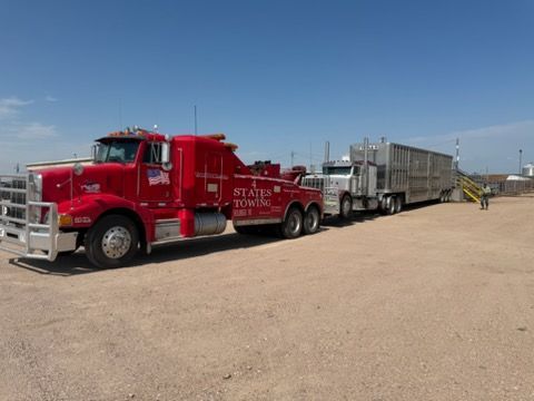 Red semi-truck hauling silver livestock trailers on a dirt lot under a clear blue sky