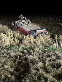 Overturned red combine harvester in a field at night under a bright light