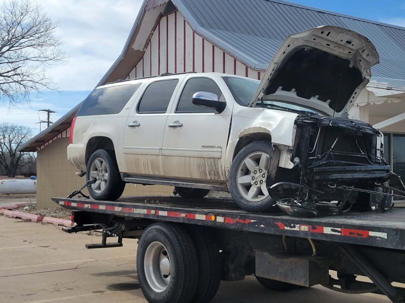 Damaged white SUV on a flatbed tow truck with front end wrecked and hood open